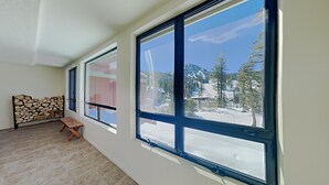A room with large windows, a wooden bench, and a stack of firewood against the wall.