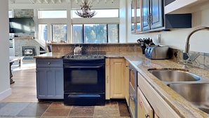A modern kitchen with a built-in oven, a stove, and a large window overlooking a forest. - Large Upgraded 4 Bedroom Condo in Mammoth! Easy access To Hot Tubs, Pool, Sauna by RedAwning (Mammoth Lakes)