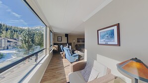 Una sala de estar moderna con un ventanal grande, una chimenea y vistas a una montaña nevada.