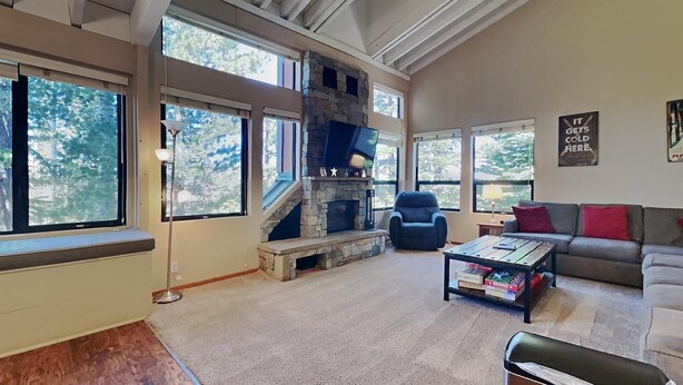 A spacious living room with a stone fireplace, large windows, a sofa, and a coffee table. - Family Friendly Spacious Mountain 4 Bedroom Condo - Closest to Canyon Lodge! by RedAwning (Mammoth Lakes)