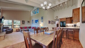 A spacious living area with a large sofa, dining table, and chairs, a kitchen with wooden cabinets, and a chandelier. - Family Friendly Spacious Mountain 4 Bedroom Condo - Closest to Canyon Lodge! by RedAwning (Mammoth Lakes)