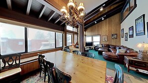 A spacious living room with a large wooden dining table, leather sofas, and a chandelier.