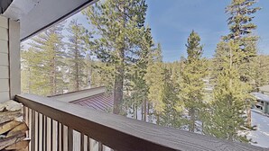 Un balcon offrant une vue sur de grands arbres à feuilles persistantes et un ciel dégagé.