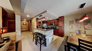 Una cocina moderna con una isla central, taburetes de bar y una zona de comedor con mesa y sillas.