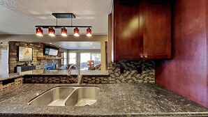 Una cocina con encimera de granito, pileta doble, salpicadero de piedra y muebles de madera.