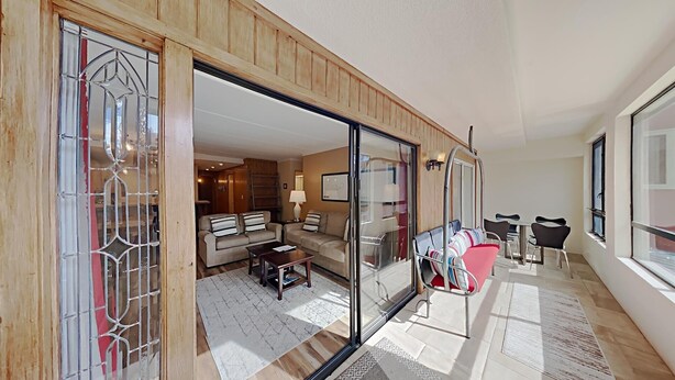 A spacious living area with a sliding glass door leading to a bedroom, a dining area with a table and chairs, and a sofa set.