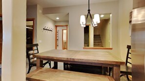A dining area with a wooden table and chairs, a hanging light fixture, and a staircase in the background. - Beautiful Mountainside 4 BR Plus Loft/4 Bath Home in Mammoth! by RedAwning (Mammoth Lakes)