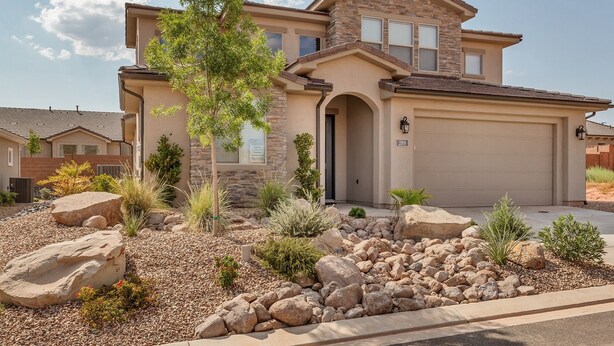 A two-story house with a stone facade, a garage, and a landscaped front yard with rocks and small trees.
