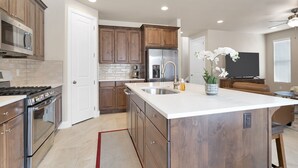 A modern kitchen with wooden cabinets, a stainless steel refrigerator, and a large island with a sink.
