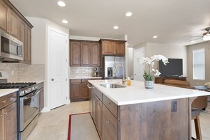 A modern kitchen with wooden cabinets, a stainless steel refrigerator, and a large island with a sink.