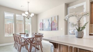 A modern kitchen with a dining area, featuring a large island, wooden chairs, and a vase of white orchids.