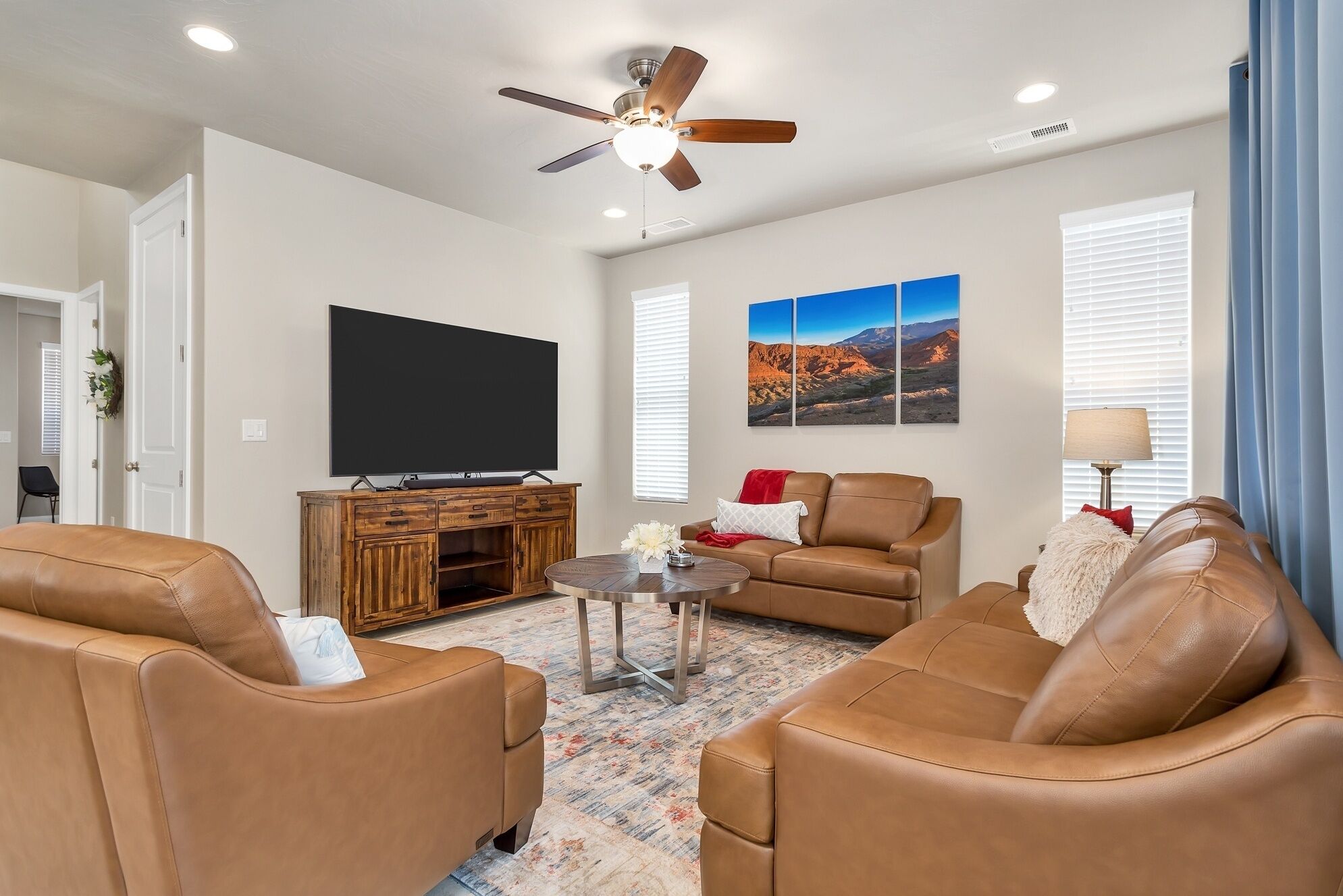 A living room with leather sofas, a flat-screen TV, a wooden cabinet, and a ceiling fan.
