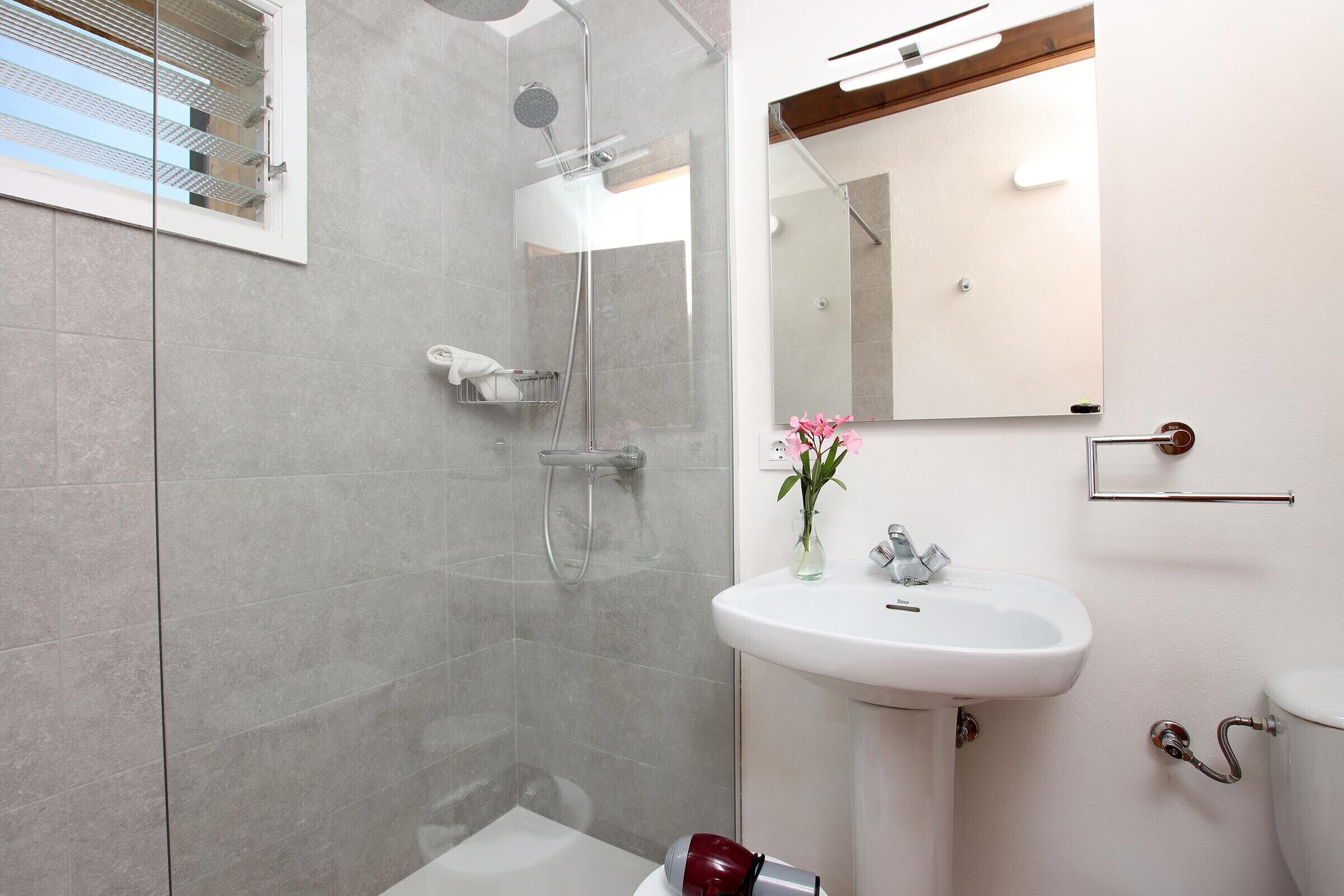 Un bagno moderno con doccia vetrata, lavandino bianco e specchio sopra.