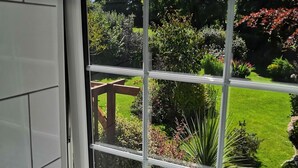 A view through a window with a wooden railing, a lawn, and various plants. - 1 Bed Cottage-sleeps 3-pool-pets-near St Ives (Camborne)