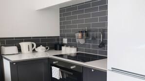 A modern kitchen with black cabinets, a white countertop, a black tiled backsplash, and stainless steel appliances. - 1 Bed Cottage-sleeps 3-pool-pets-near St Ives (Camborne)