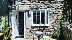 A stone house with a wooden deck, a table with chairs, and a window with blinds. - 1 Bed Cottage-sleeps 3-pool-pets-near St Ives (Camborne)
