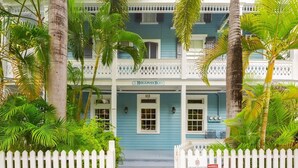 A two-story building with a blue facade, white balcony railings, and a white picket fence. - Sky Loft - Steps from Duval Street & Shared Pool (Key West)