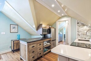 A modern kitchen with a wooden countertop, a microwave, and a refrigerator. There is a small island with drawers and a vase. The kitchen has a view of the living area through an open door. - Sky Loft - Steps from Duval Street & Shared Pool (Key West)
