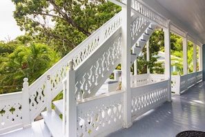 A white wooden staircase with intricate cut-out designs, leading to a covered outdoor area with a view of lush greenery. - Sky Loft - Steps from Duval Street & Shared Pool (Key West)