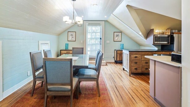 A dining area with a table and chairs, a kitchen with appliances, and a window with blinds.