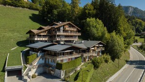 Ein großes, mehrstöckiges Chalet mit Balkon, an einem Hang mit einer nahegelegenen Straße gelegen.
