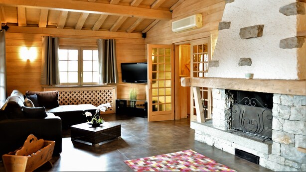 Ein gemütliches Wohnzimmer mit Kamin aus Stein, Holzbalken, einem Fernseher und einem bequemen Sofa.