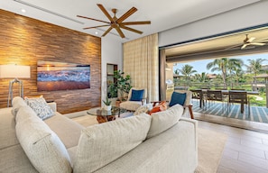 Un salon moderne avec un mur en bois, un ventilateur de plafond, un grand téléviseur et une vue sur un paysage tropical.