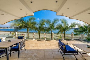 A terrace with a view of the beach, featuring a table, chairs, and decorative statues.