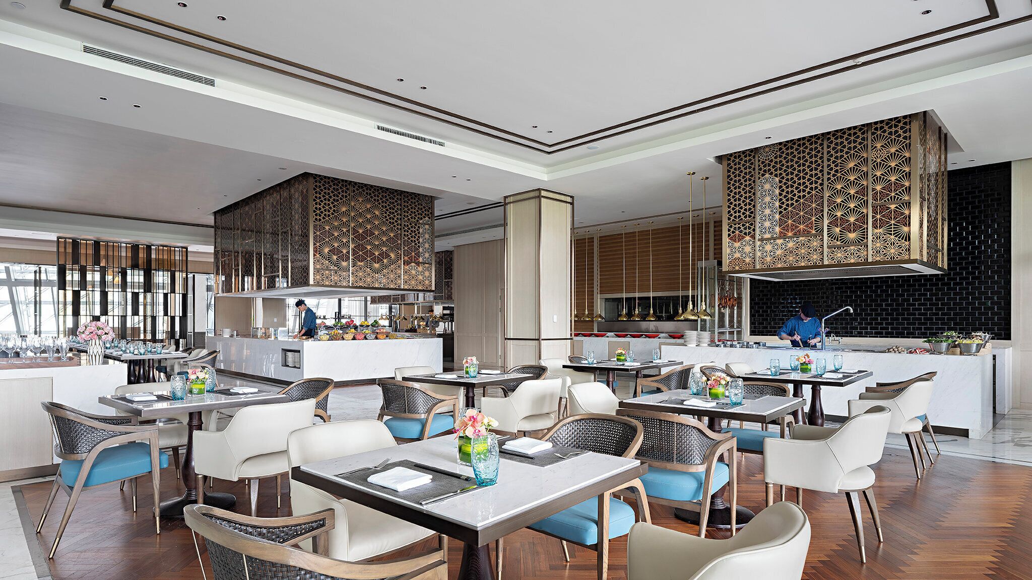 A modern restaurant with a central bar, high ceilings, and patterned wall panels.
