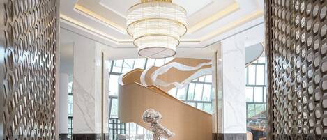 Un vestíbulo espacioso con una gran araña, piso de mármol y una escultura moderna.