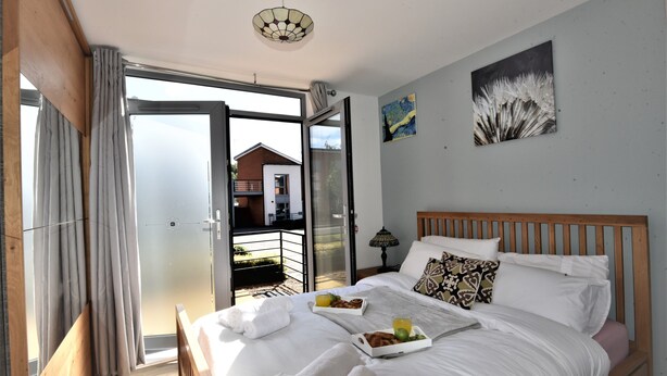 Ein Schlafzimmer mit einem Bett, einem Frühstücksbrett und Blick auf ein Haus durch eine offene Tür.