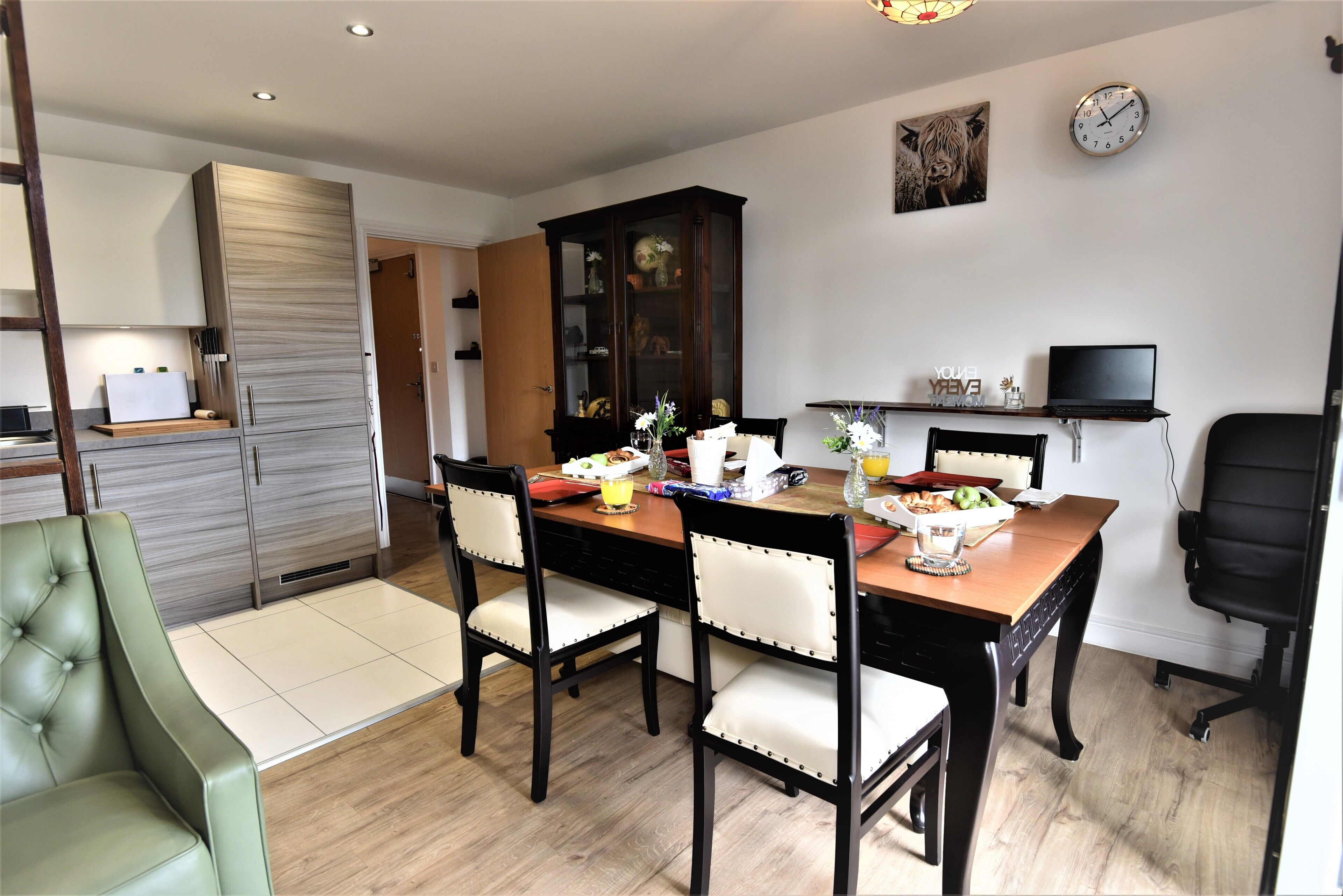 A dining area with a wooden table, four chairs, and a laptop on a shelf.
