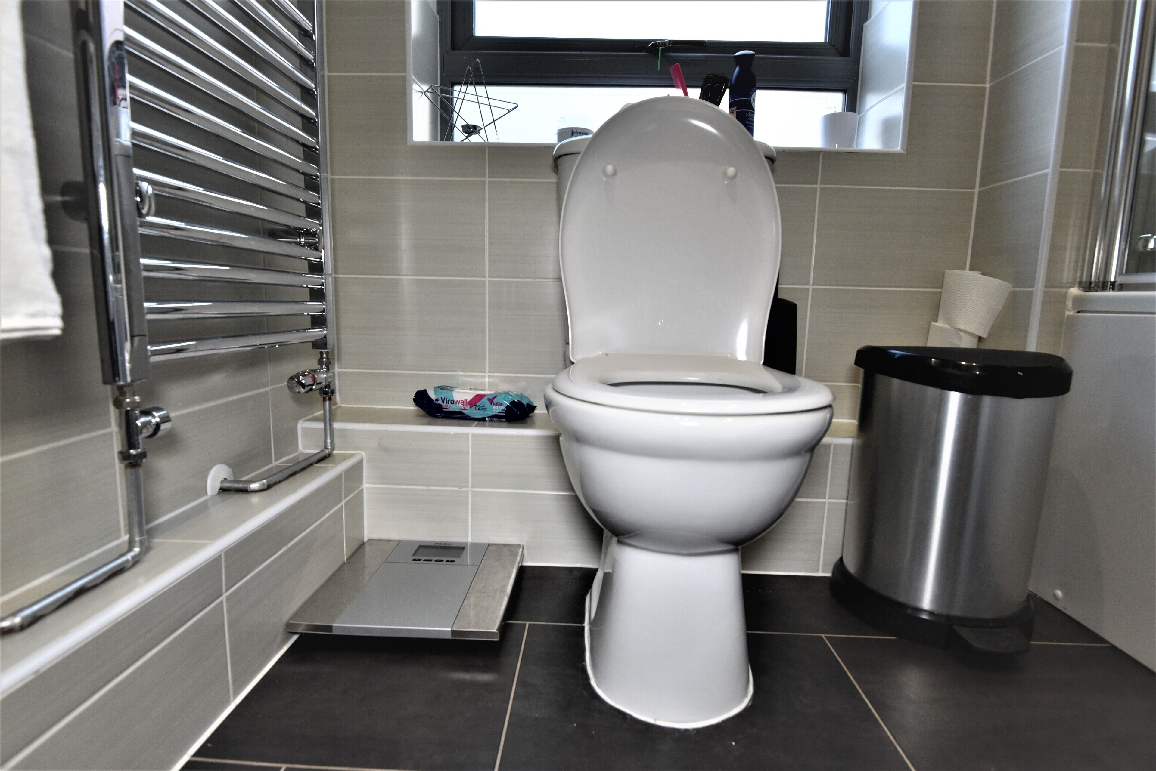 Une salle de bain moderne équipée de toilettes, d’un bidet, d’une poubelle et d’une fenêtre située au-dessus des toilettes.