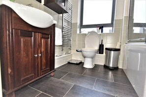 Een moderne badkamer met een houten wastafelmeubel, een wit toilet en een roestvrijstalen prullenbak.