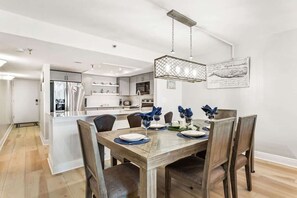 A modern kitchen with white cabinetry, a dining area with a wooden table and chairs, and a hanging light fixture.