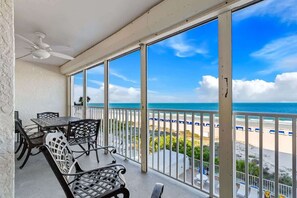 A balcony with a table and chairs, a ceiling fan, and a view of the beach and ocean. - Sea Gem Beachfront Condo in Indian Shores (Indian Shores)