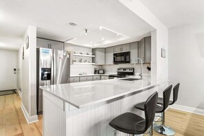 Una cocina moderna con una isla central, electrodomésticos de acero inoxidable y taburetes de bar.
