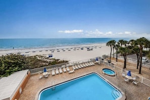 Un área de piscina con sillones y sombrillas, una playa con sombrillas y palmeras.