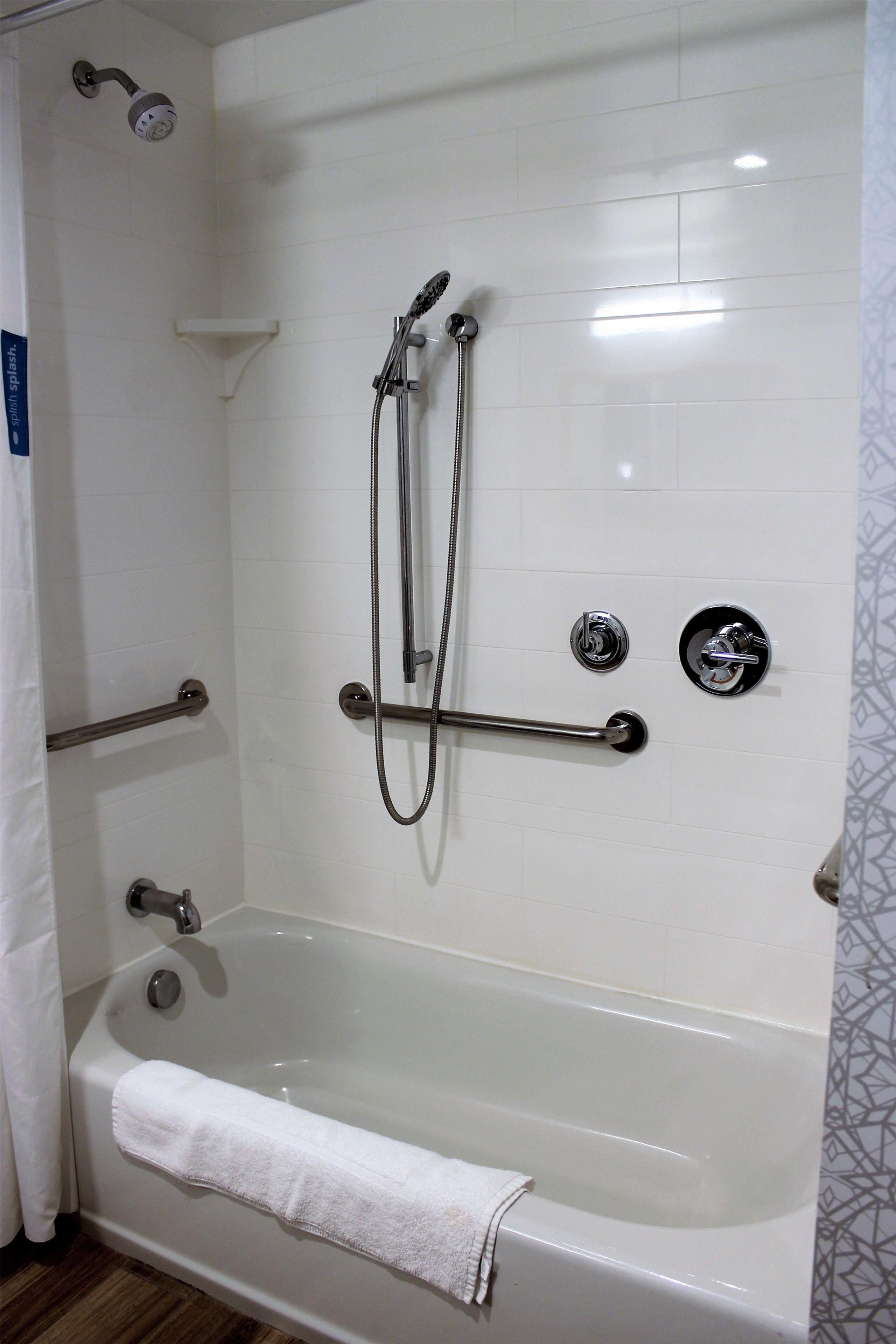 Un baño con bañera, cabezal de ducha y barandilla.