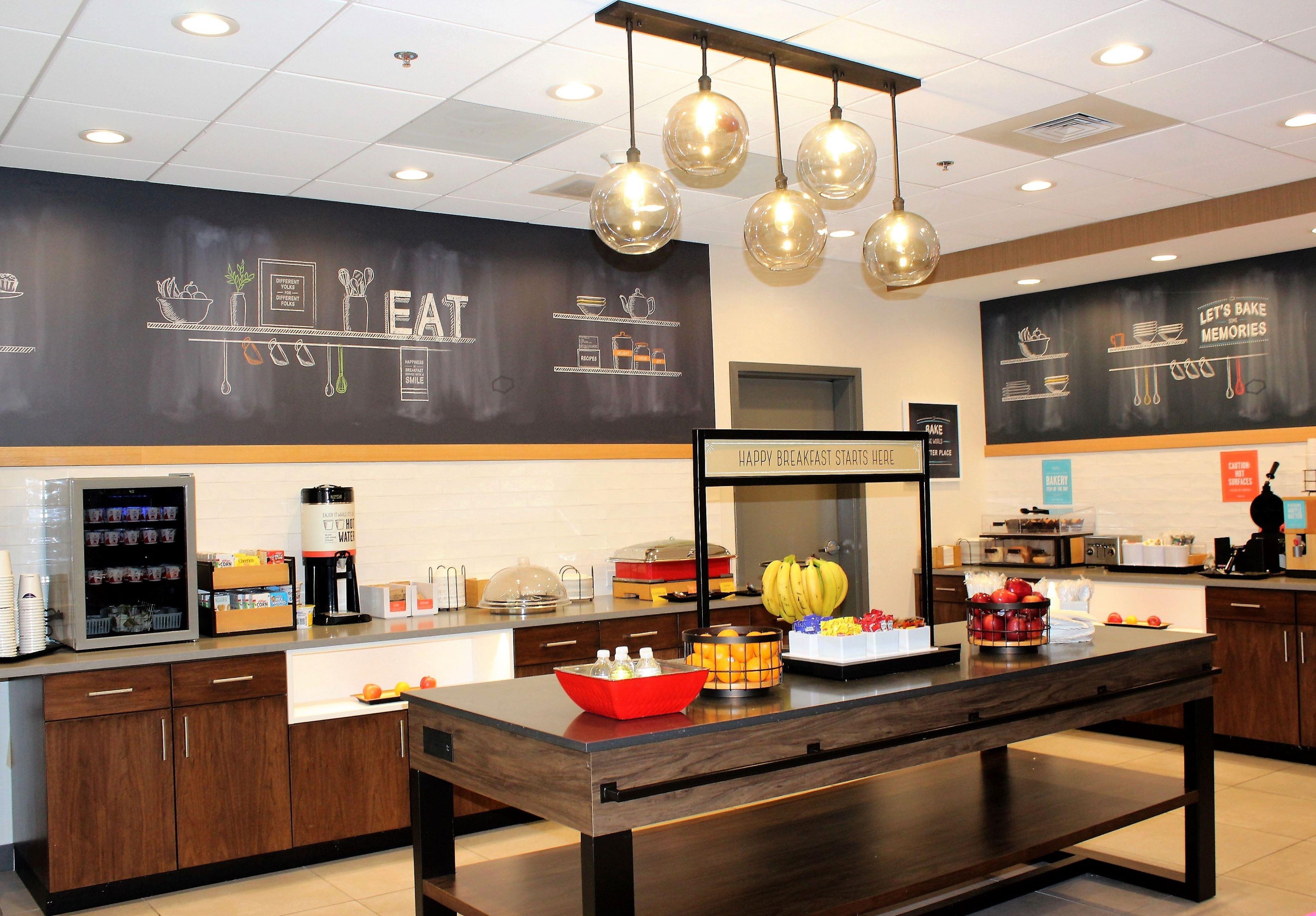 A breakfast buffet area with a variety of food items, a coffee station, and a chalkboard with kitchen-related drawings.