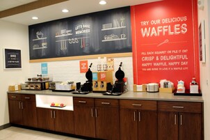 A kitchen counter with waffle-making equipment and a sign promoting waffles.
