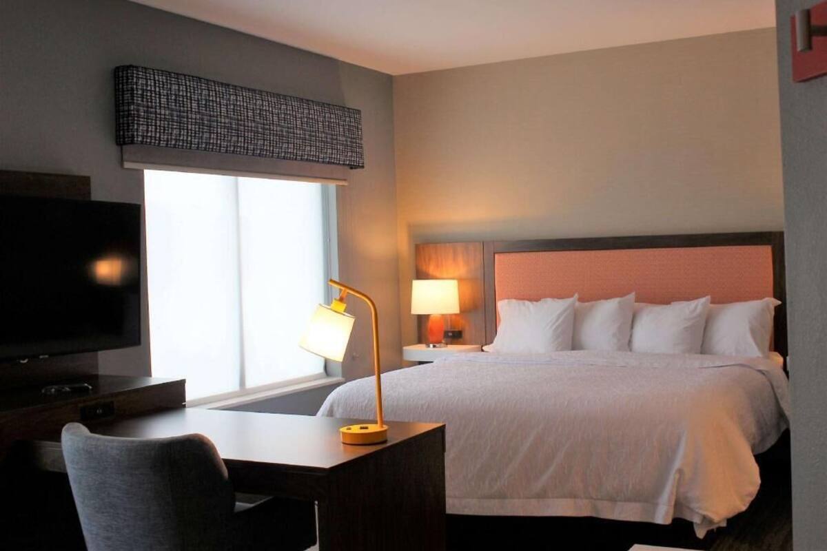 A hotel room with a bed, a desk, a television, a lamp, and a window.