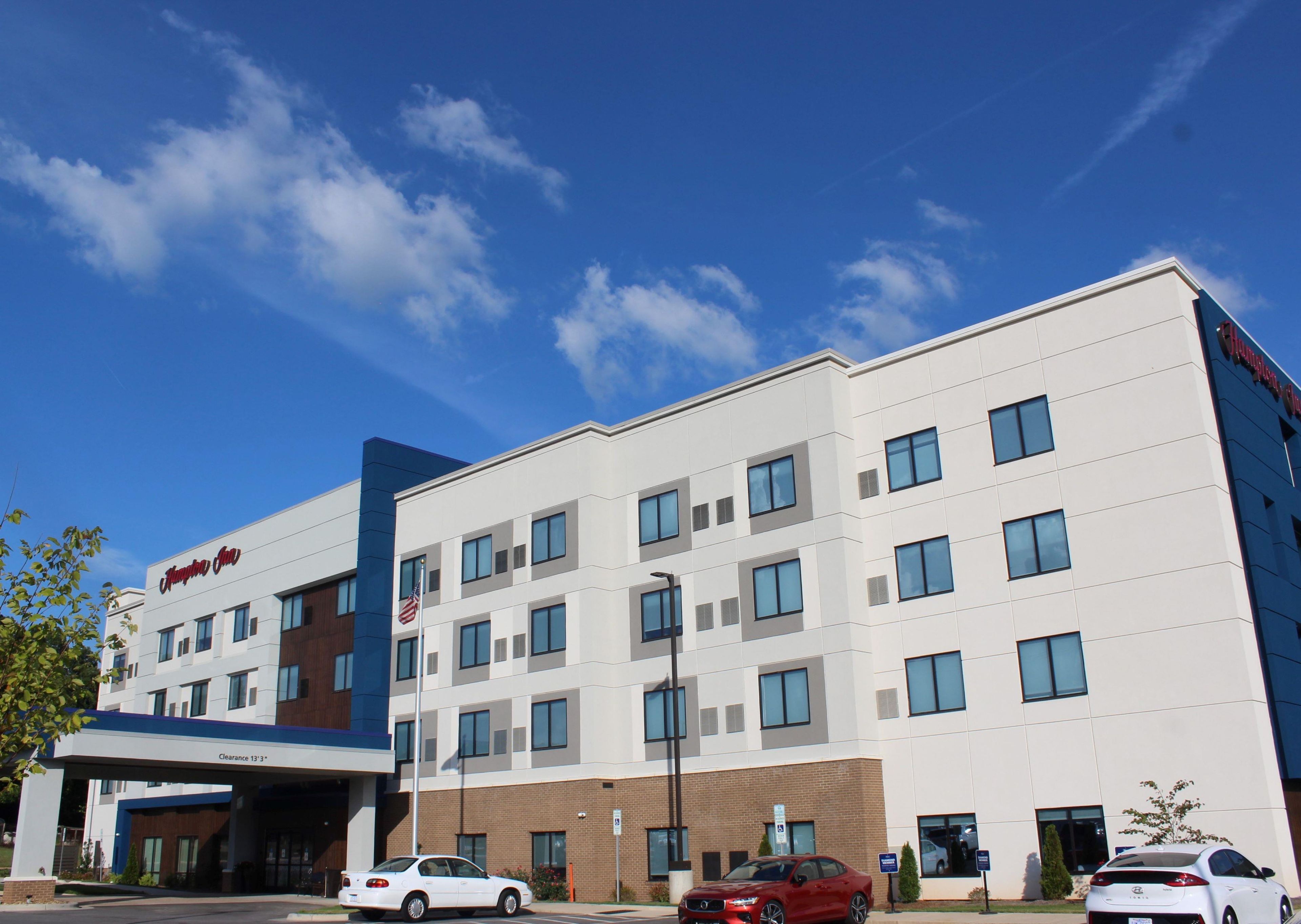A modern hotel with a clear sky, multiple windows, and a parking area with cars.