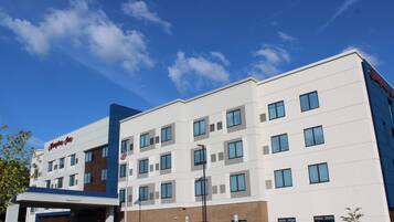 A modern hotel with a clear sky, multiple windows, and a parking area with cars.