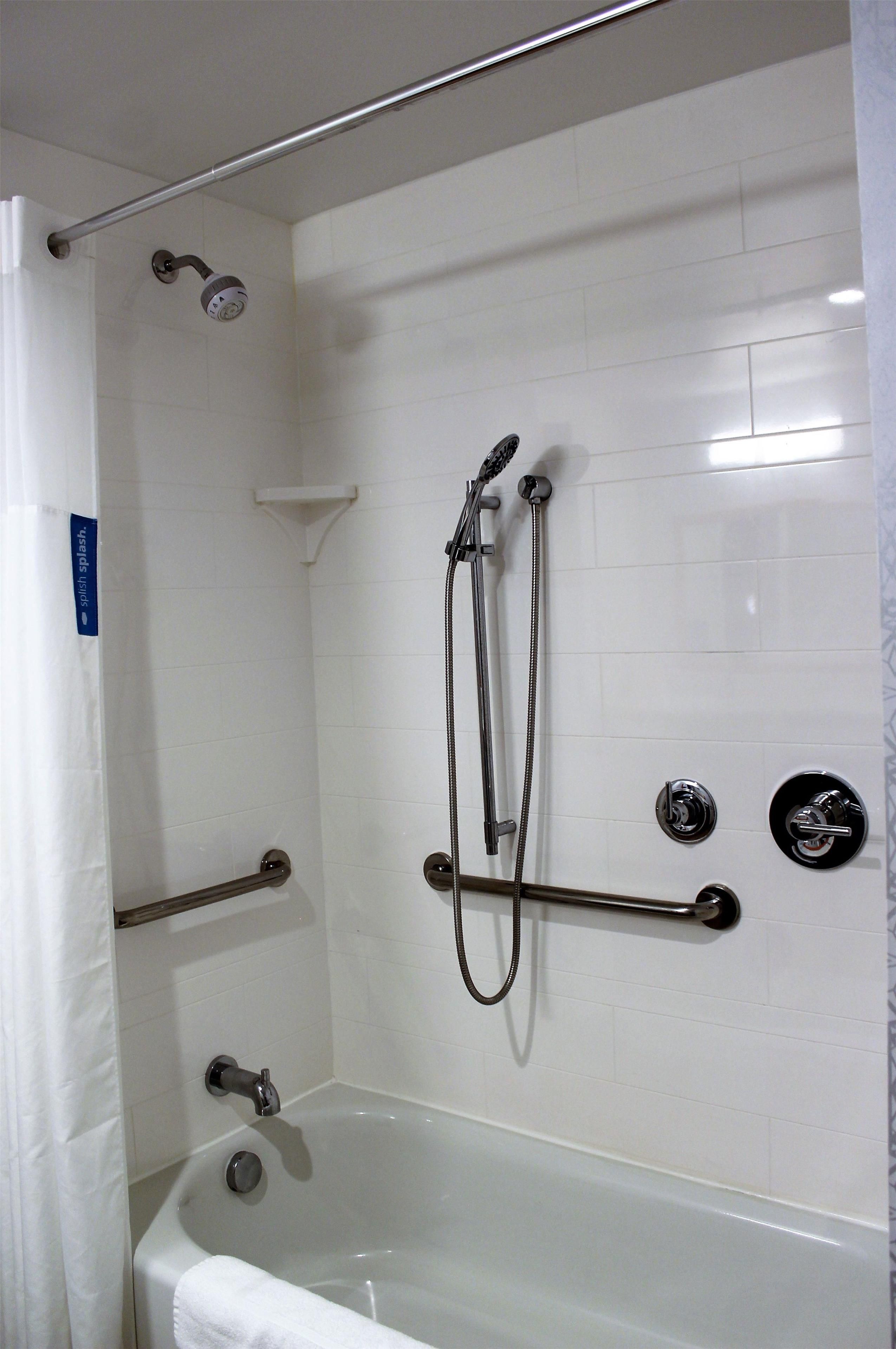 A bathroom with a bathtub, a shower with a handheld showerhead, and grab bars.