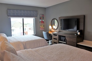 Une chambre d’hôtel avec deux lits, un bureau avec un ordinateur, une télévision et une grande fenêtre.