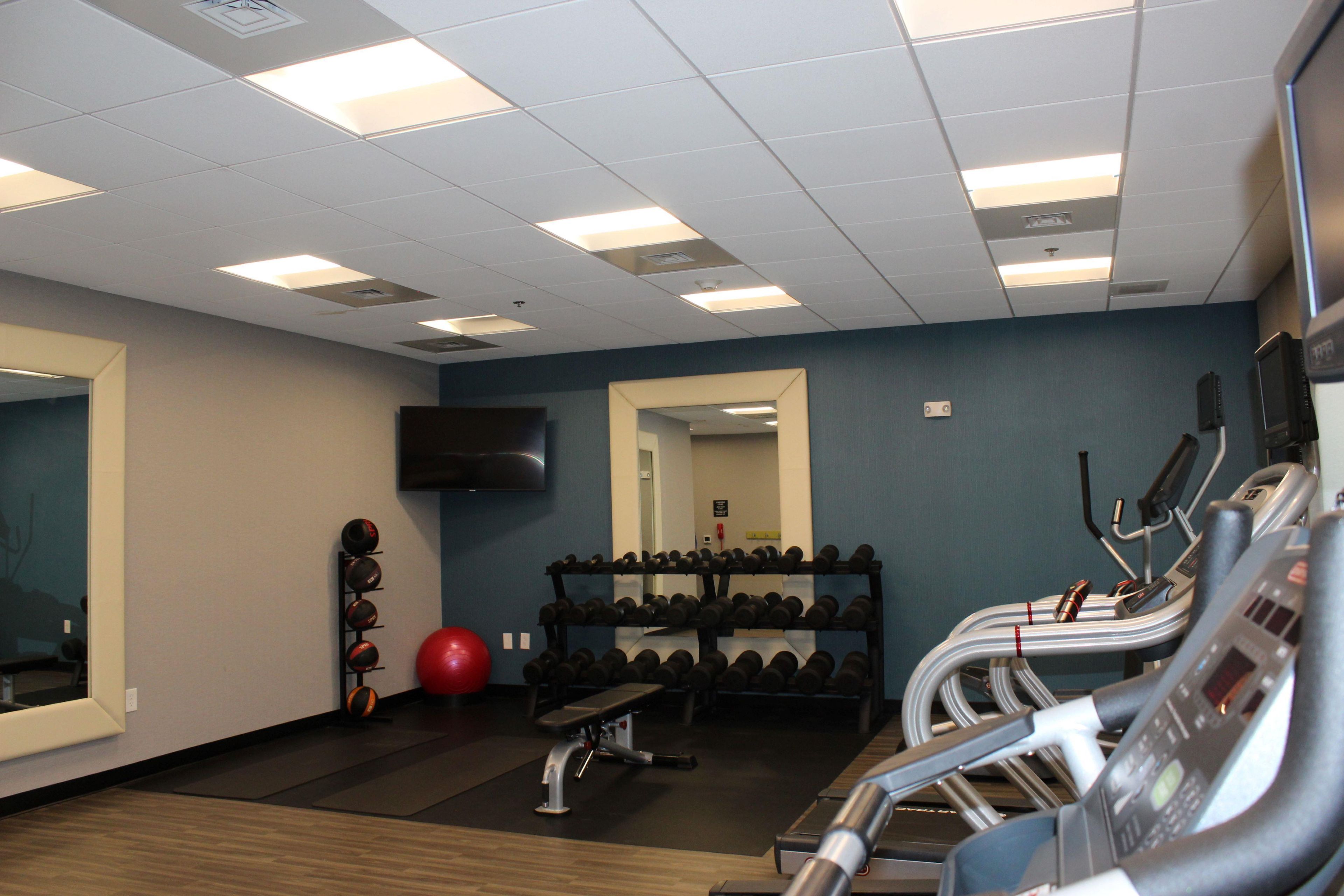 A gym with exercise equipment, a mirror, and a television on the wall.