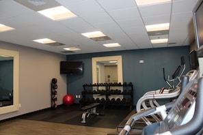 Une salle de sport équipée de matériel d’exercice, avec un miroir et un téléviseur accroché au mur.