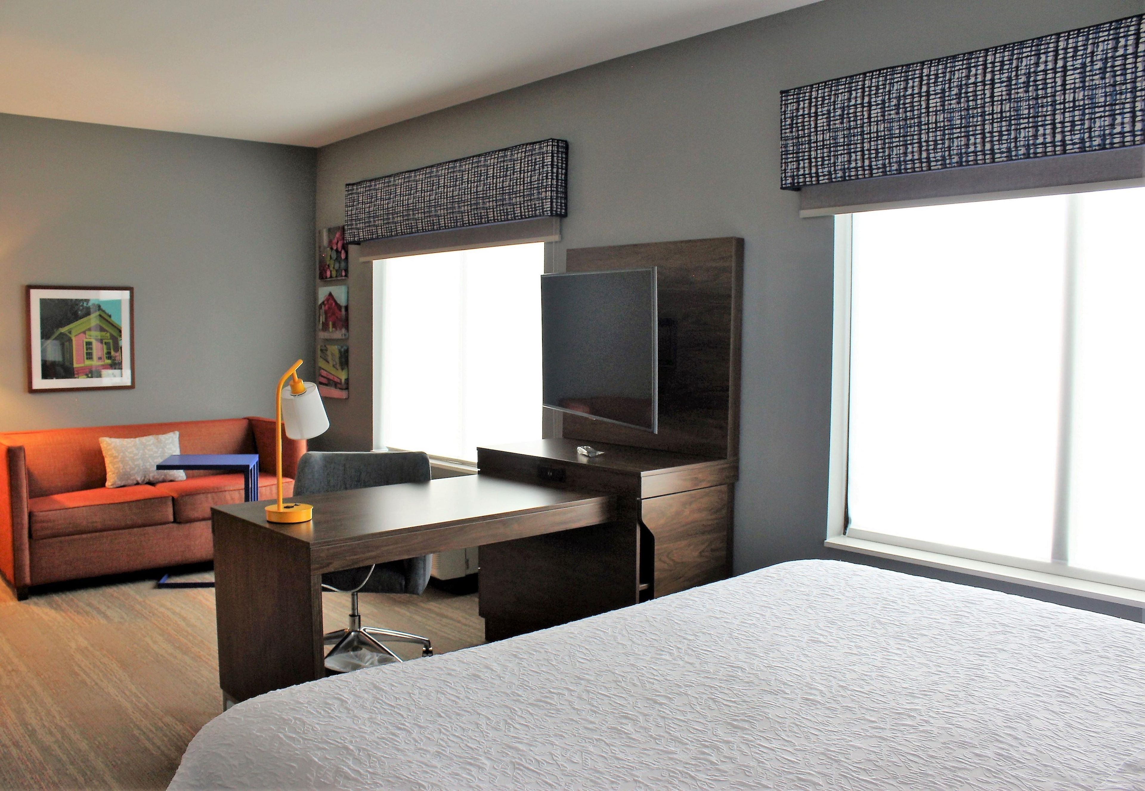 A hotel room with a bed, a desk with a chair, a television, and a sofa.