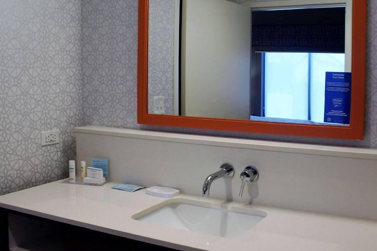 A bathroom with a large mirror, two sinks, a towel rack, and a window with a view.